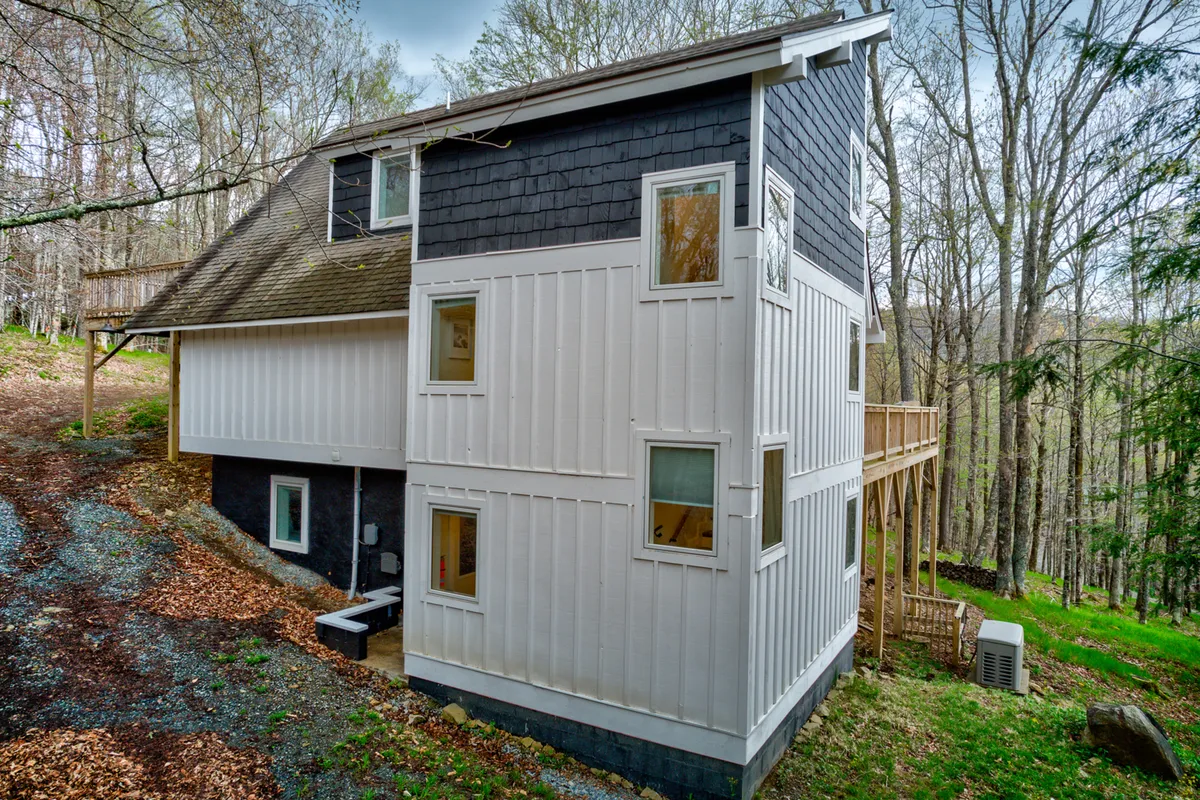 A cozy wooden deck attached to the home, framed by slate-colored siding and white paneling, and surrounded by tranquil forest. The space looks perfect for unwinding after a day on the slopes, offering a seamless transition from outdoor pursuits to relaxation at home.
