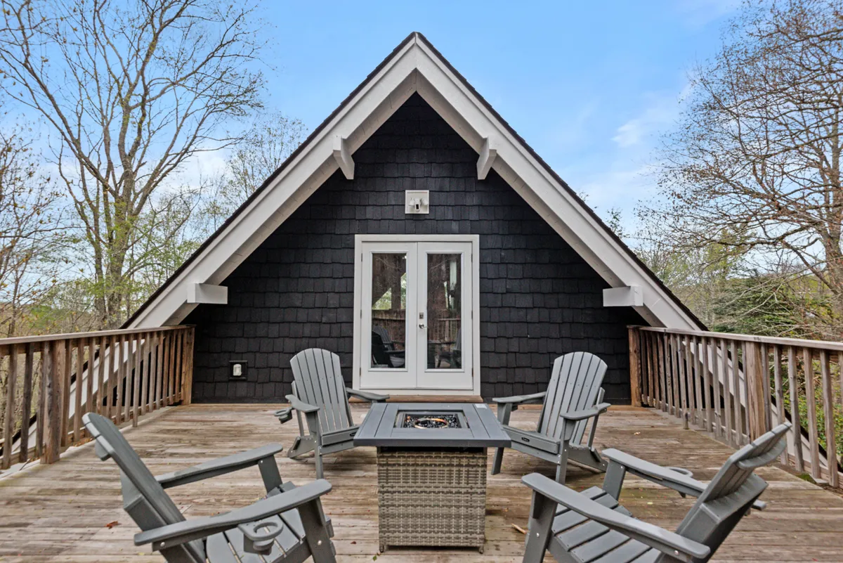 A private deck with a firepit, Adirondack chairs, and a sloped roof overhead, surrounded by trees. The area radiates warmth and is set up for starlit evenings, group conversations, and enjoying the mountain air after a day of adventure.