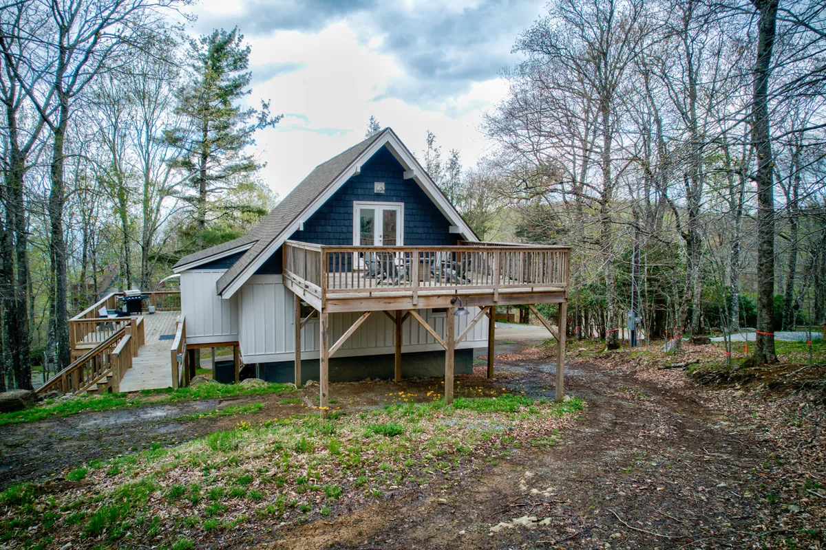 A tranquil scene featuring a wooden deck attached to an A-frame home, framed by towering trees. The deck is sunlit, inviting for morning coffee or sunset relaxation, and exudes a sense of immersion in nature.