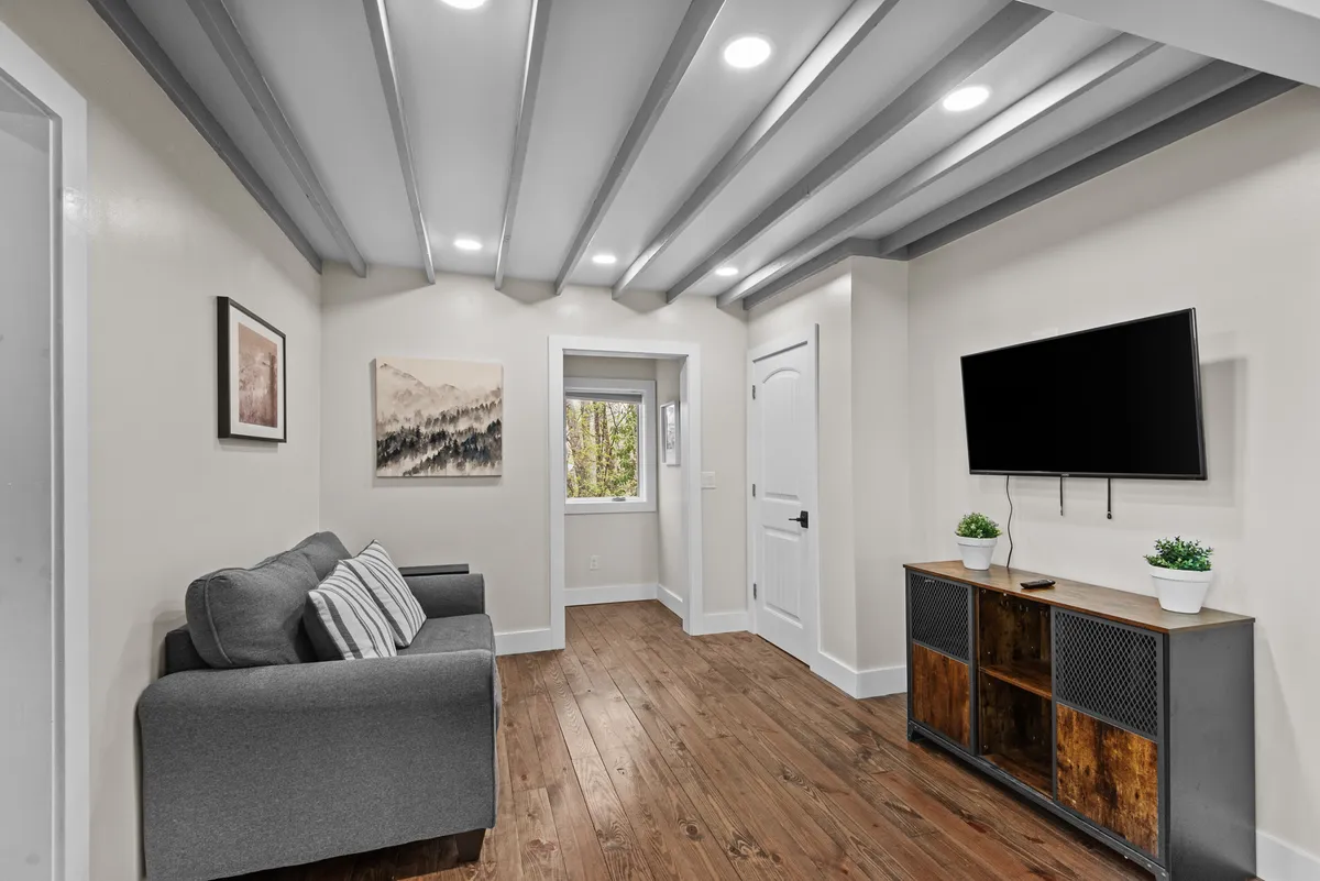 A plush, modern family room with a comfortable sofa, a smart TV mounted across, artwork for a homey feel, and a window framing the outdoors. The ambiance is both cozy and contemporary, ideal for relaxing after adventures or sharing laughter during game nights.