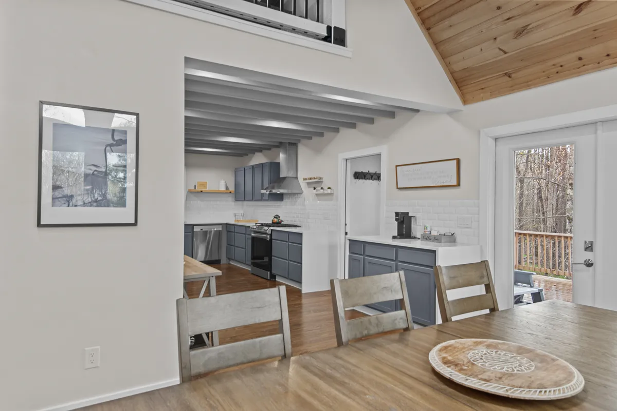 This inviting kitchen and dining area features modern cabinetry, a dining table, large windows, and classic wooden ceiling beams. The layout is ideal for preparing and enjoying meals together after a day of exploring local cuisine.