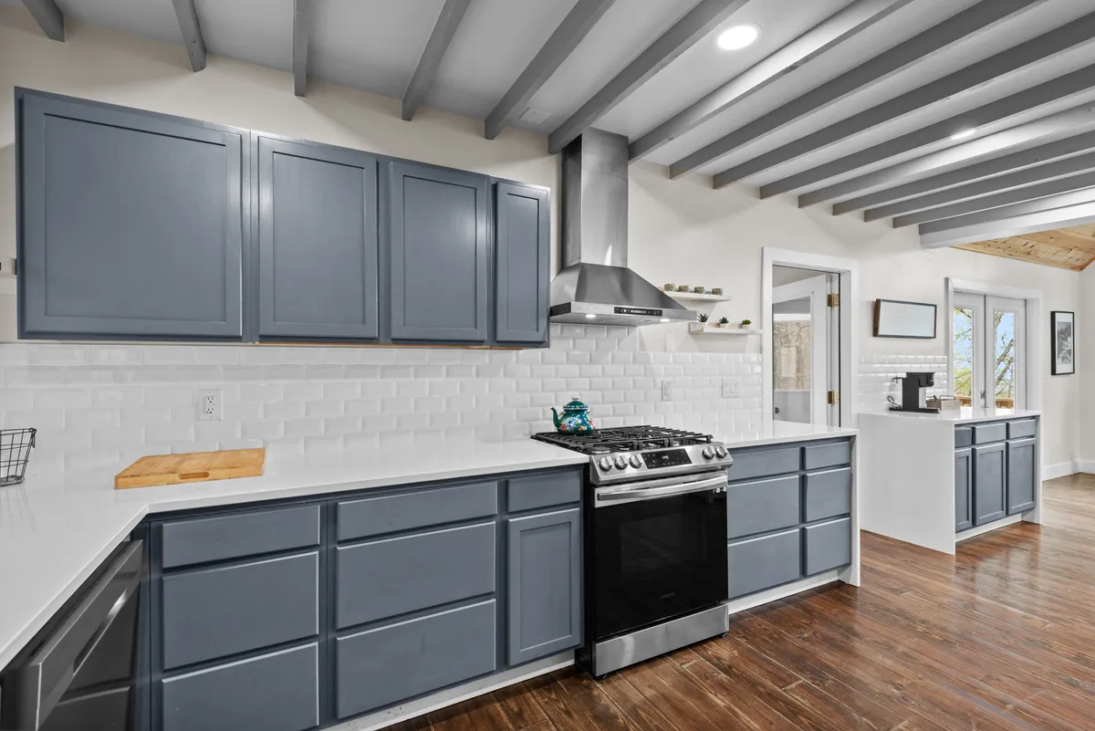A modern kitchen with a large island, stainless steel appliances, blue cabinetry, and a white tiled backsplash. The open space is designed for cooking together, socializing, or preparing celebratory meals.