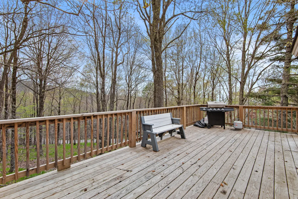 This exterior image features a spacious deck with a wooden bench, a grill, and trees in the background. The setup suggests a perfect spot for relaxing outdoors, enjoying nature, or gathering for a barbecue with friends and family.