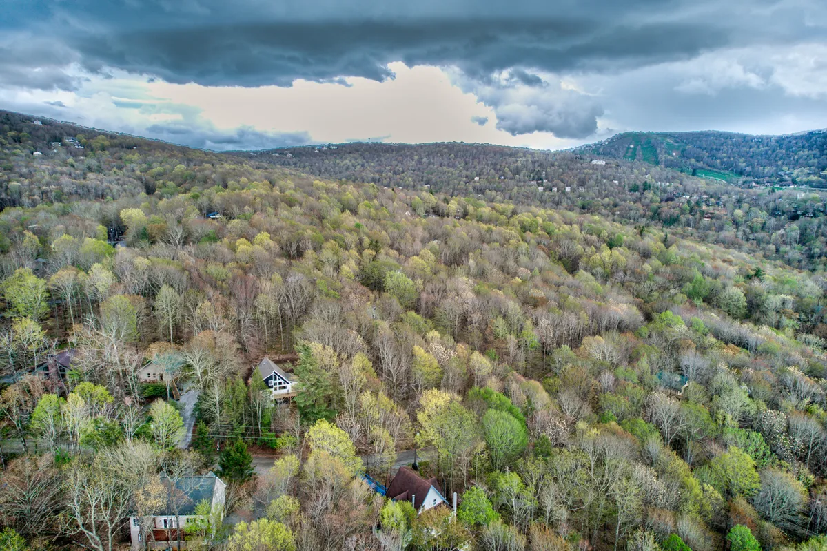 A sweeping view of distant mountains dotted with scattered houses and surrounded by dense forest. The landscape is blanketed in serenity, inviting thoughts of outdoor winter adventures and the allure of Beech Mountain's slopes just beyond view.