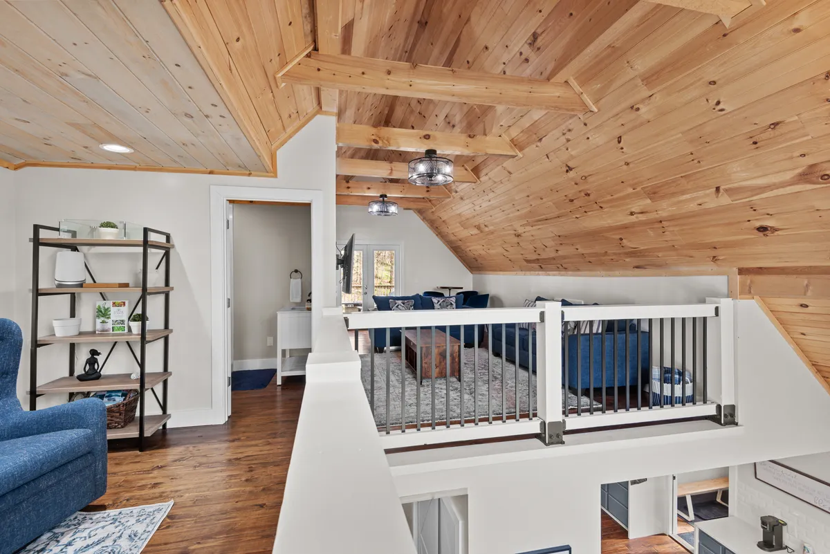 A stylish loft lounge with blue seating, a wooden ceiling, modern metal light fixtures, and decorative shelving. The setting is intimate and designed for both socializing and relaxing, capturing a retreat-like ambiance ideal for post-adventure unwinding.