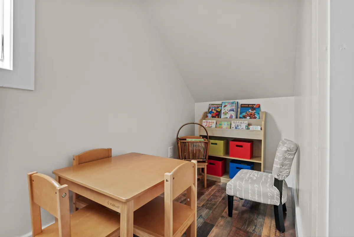 A cheerful kids’ nook with a child-sized wooden table, colorful storage bins, a bookshelf filled with children's books, and an accent chair. The setup is bright and nurturing, perfect for play, reading, or creative activities.